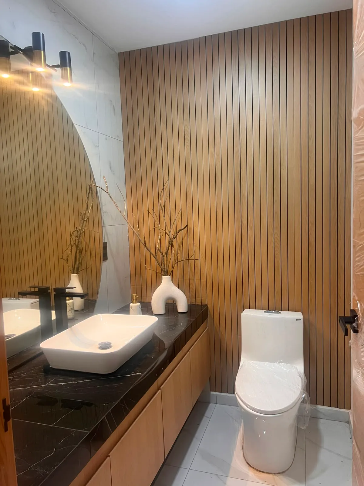 Baño en Morelia con lambrín vertical de madera, cubierta de mármol negro y lavabos sobre cubierta